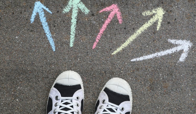 Verschillende gekleurde pijlen op asfaltvloer met gymschoenen die keuzes symboliseren.