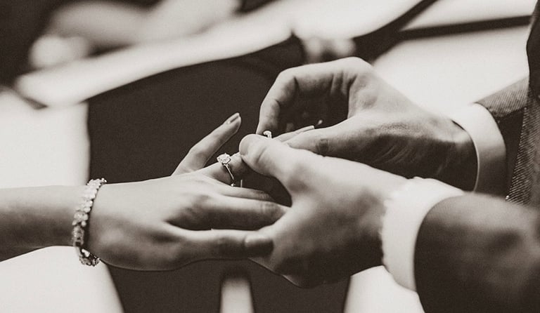 A groom sliding a diamond wedding band onto the bride's finger during a classic ceremony.