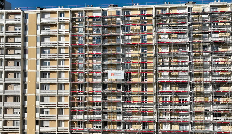 Multi-story apartment building renovation with metal scaffolding for exterior facade construction.