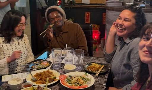 Diverse friends laughing and eating Thai food at a restaurant with noodles and rice dishes.
