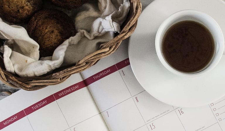 Calendar with cup of coffee and muffins on white table