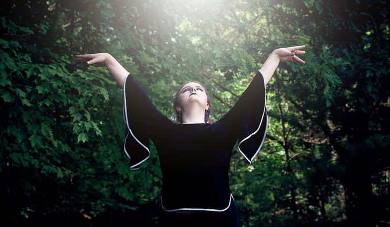 a woman with her arms outstretched up and she is looking up to the sun in the forest