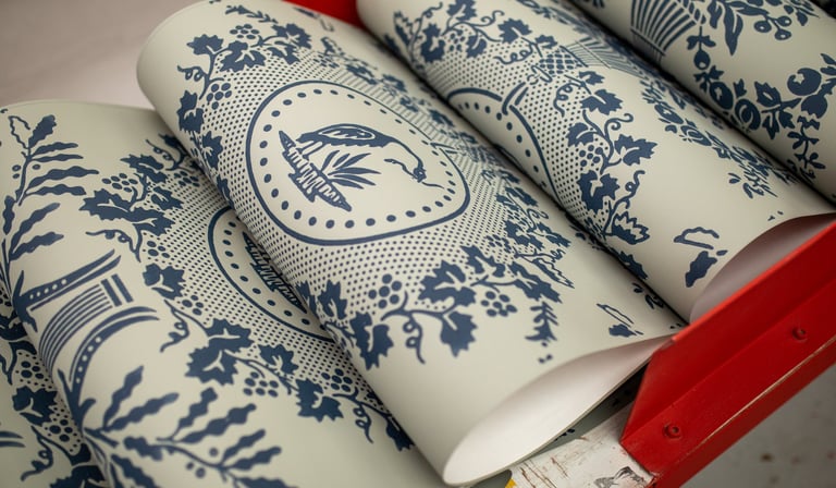 Rolls of vintage blue and white toile wallpaper with floral and bird patterns in a red rack.