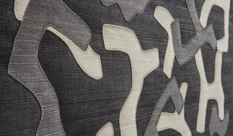 Close-up of grey and white textured fabric with abstract appliqué shapes for modern interior design.