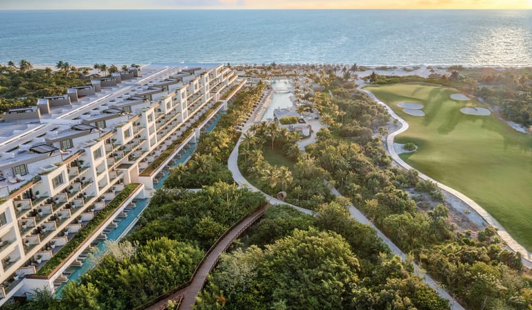Aerial view of a luxury beachfront resort with a golf course and tropical gardens at sunset.