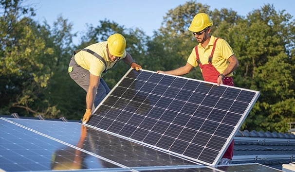Two technicians in hard hats installing solar panels on a residential rooftop for renewable energy.