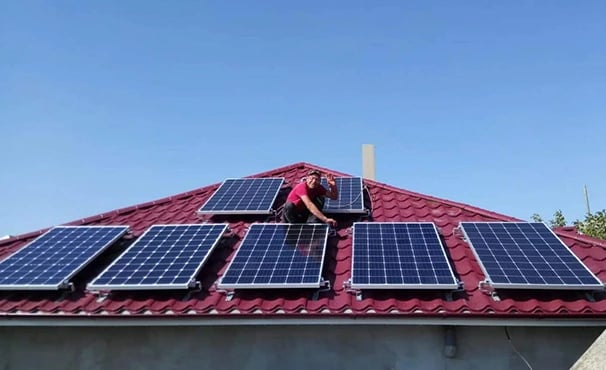 Professional technician installing solar panels on a residential red metal tile roof for renewable energy.