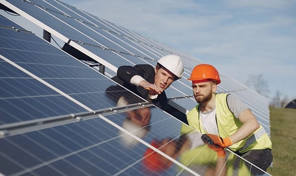 Engineers in hard hats inspecting a solar panel farm installation for renewable energy.