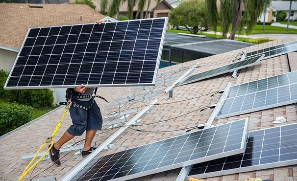 Professional technician installing a residential solar panel system on a shingle roof.