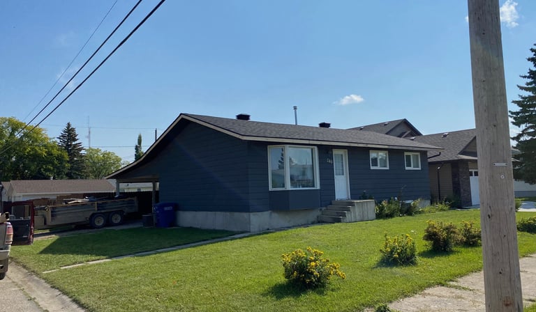 A modern charcoal grey bungalow house with a green lawn and blue sky on a suburban street.