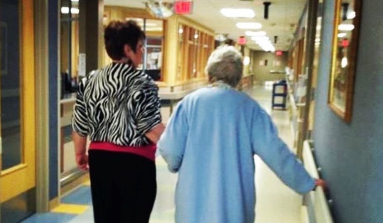 Photo of Debbie escorting her mother down a medical hallway.