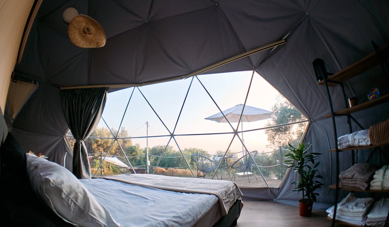 Unutrašnjost glamping kupole sa pogledom na more i udobnim krevetom