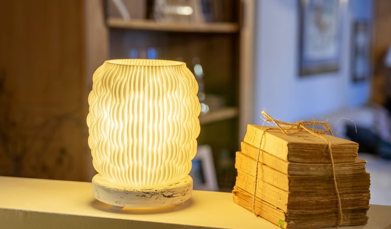 A warm, 3D printed textured lamp glowing next to a stack of vintage books on a shelf.