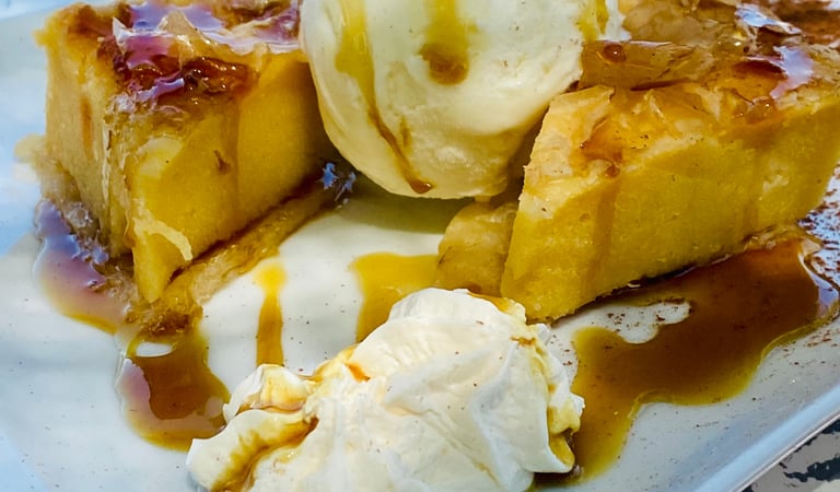 Warm Greek orange cake served with vanilla ice cream and honey syrup on a white plate.