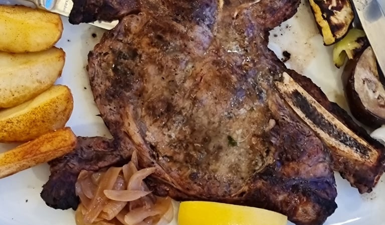 Grilled t-bone steak served with potato wedges, caramelized onions, and a side of creamy polenta.