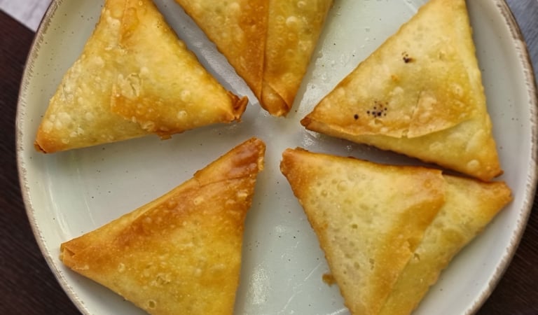 A plate of five golden-brown, crispy triangular vegetable samosas arranged in a circle.