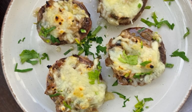 Four cheesy stuffed mushrooms garnished with fresh herbs on a white ceramic plate.