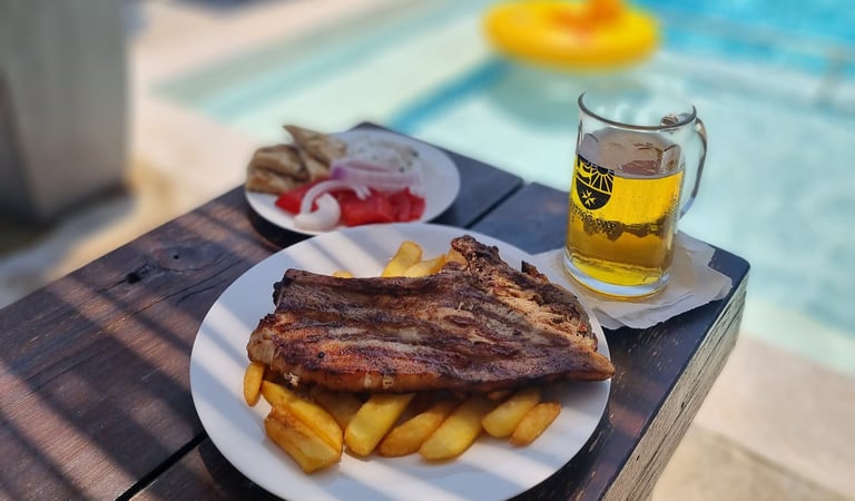 Grilled pork steak and french fries served with cold beer by a sunny swimming pool.