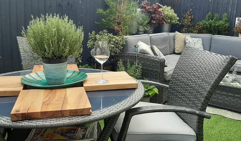 Modern garden patio with grey rattan furnituree, potted herbs, and a glass of wine on a table.