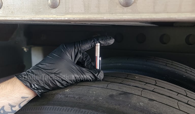 A gloved technician uses a tire depth gauge to check the tread on a semi-trailer tire.