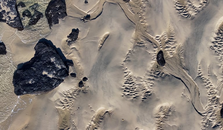 Vue aérienne de motifs de sable de plage texturés avec des roches volcaniques sombres