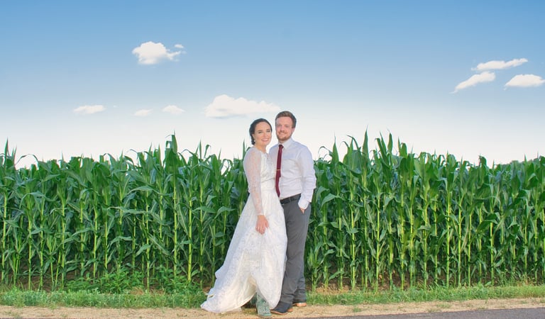 a bride and groom standing in front of a corn field