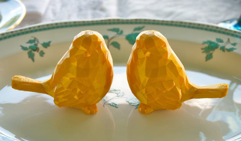 two golden bird ornaments sitting on a plate as wedding decoration