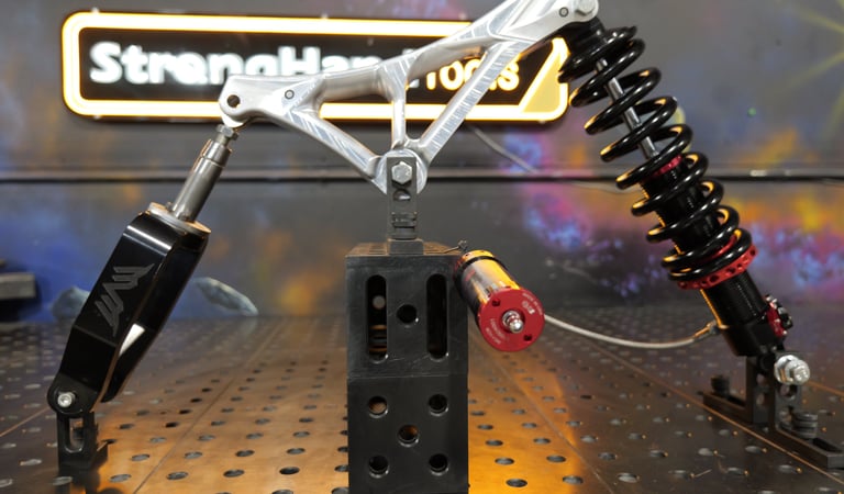 Custom CNC machined suspension linkage with a coilover shock on a welding fixture table.
