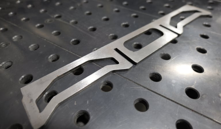 Precision laser cut metal part resting on a heavy-duty industrial welding table.