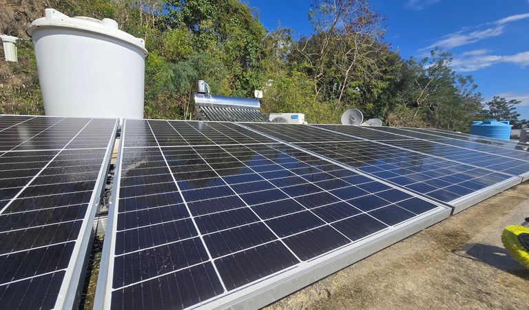 Photovoltaic solar panels installed on a rooftop with a water tank and solar heater under a clear blue sky.