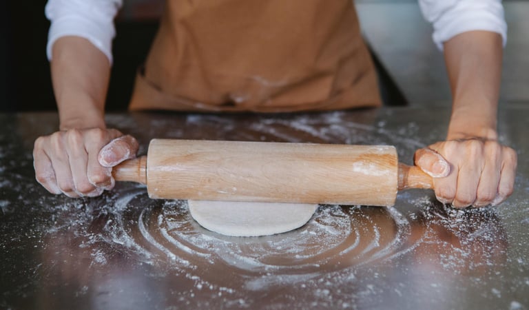 Panadero estirando masa sobre una superficie metálica enharinada con un rodillo de madera
