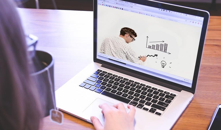 A person watching an online business presentation with charts on a silver laptop computer.