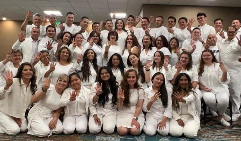 A large group of people in white clothing posing together and holding up four fingers for a photo.