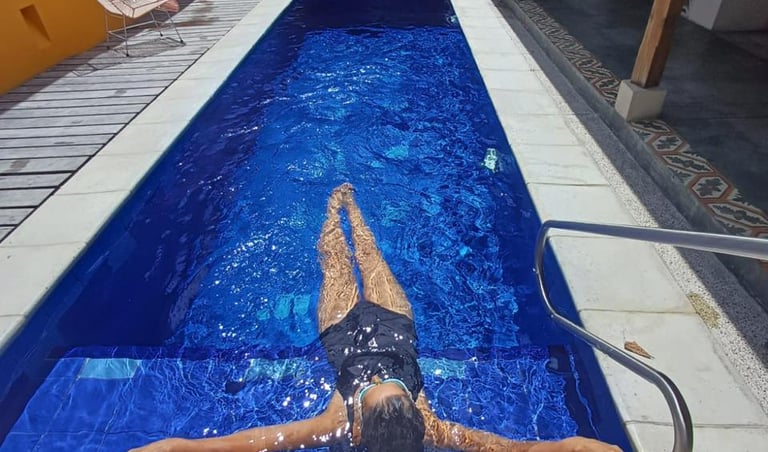 A woman floating in a luxury outdoor lap pool with deep blue water at a tropical villa.