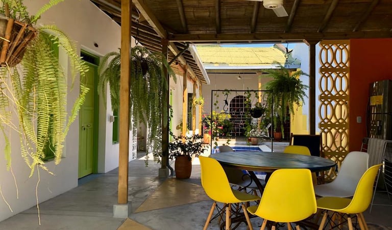 Tropical outdoor patio with yellow chairs, hanging fern plants, and a rustic bamboo roof.