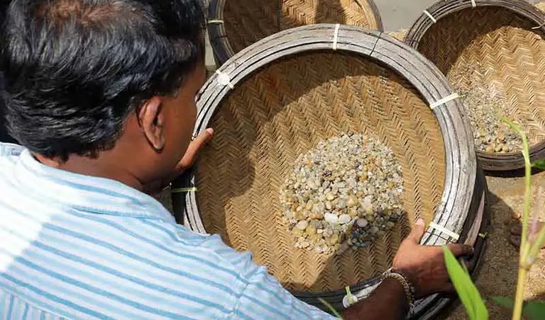 a gem miner is sorting out the gemstones using a wooden sieve.