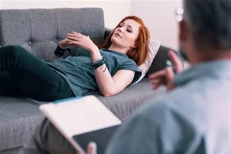 femme allongée sur un canapé en état d'hypnose et son thérapeute de dos qui la guide