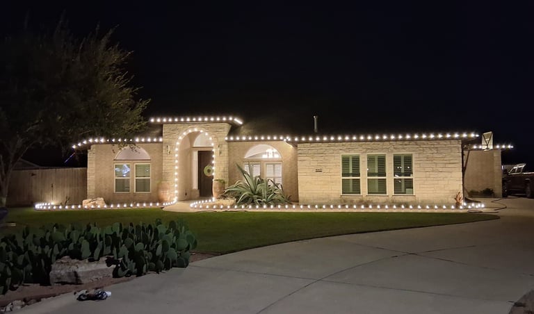 A single-story stone house at night decorated with white Christmas roofline lights in corpus christi