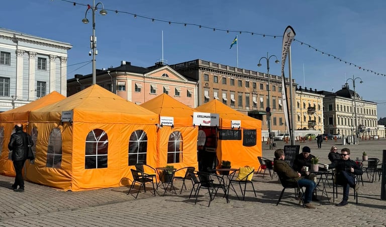a group of people sitting around tables outside orange tents