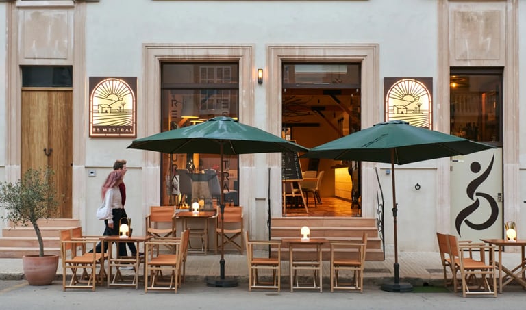 Mesas, sombrillas y cartel de Es Mestral, bajo la fachada principal del restaurante en Ses Salines.