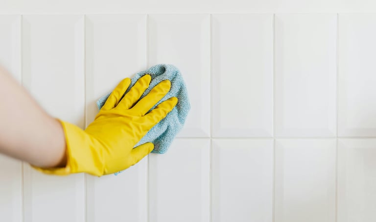 Yellow-gloved hand scrubbing grout on white tile during a professional grout cleaning service
