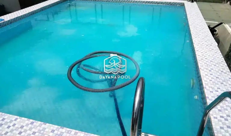 Pekerja sedang membersihkan kolam renang dengan vakum.