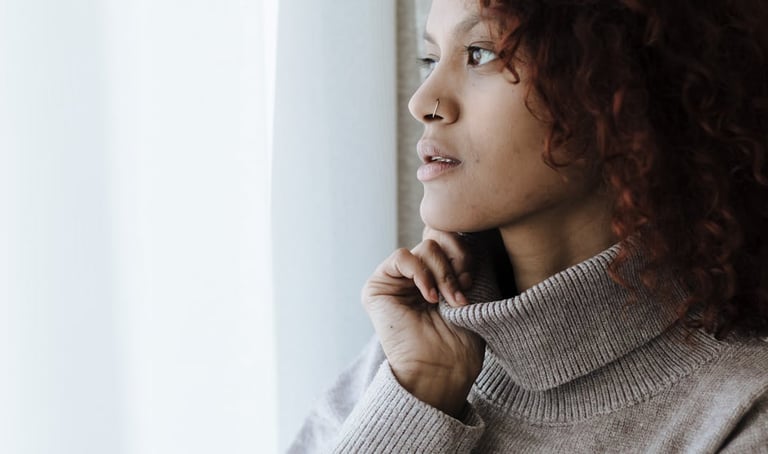 Woman in turtleneck looking thoughtfully out of a window