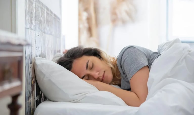 Mulher dormindo tranquilamente em cama com lençóis brancos, representando a importância do sono 