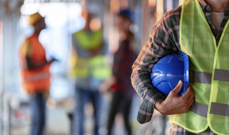 Man wearing a safety vest and holding a hard hat standing in front of other workers