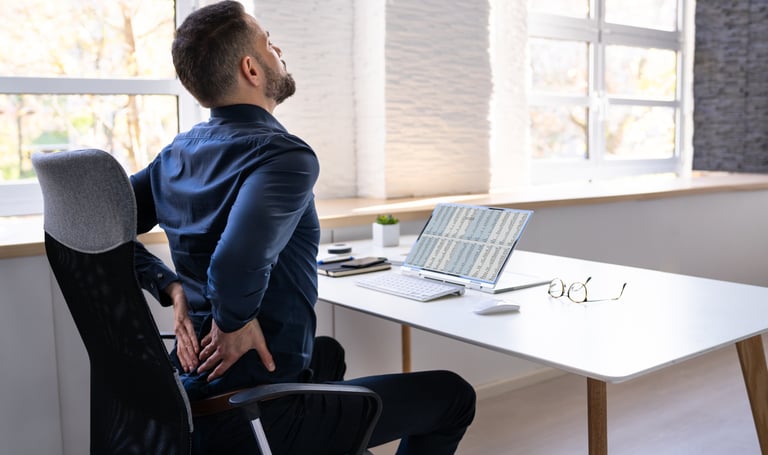 Man sitting at his desk holding his back in apparent pain