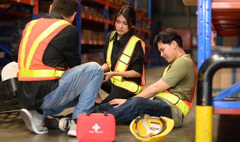 Man sitting on the ground at his workplace who has suffered an injury with coworkers assisting
