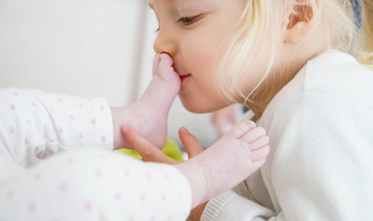 un enfant fais un bisou sur le pied d'un bébé lors d'une séance photo