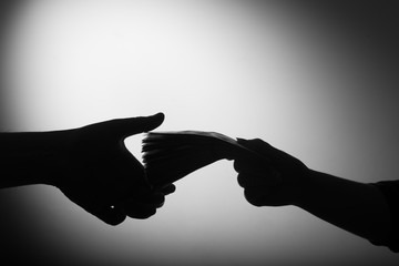 Silhouette of hands exchanging a stack of cash for a financial transaction or bribe.