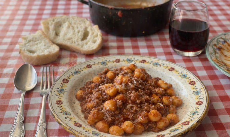 Homemade potato gnocchi with savory meat bolognese sauce served with red wine and crusty bread.
